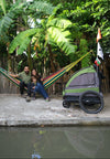 Family sitting on a wooden dock with a colorful hammock and a green and black bike trailer in the background.