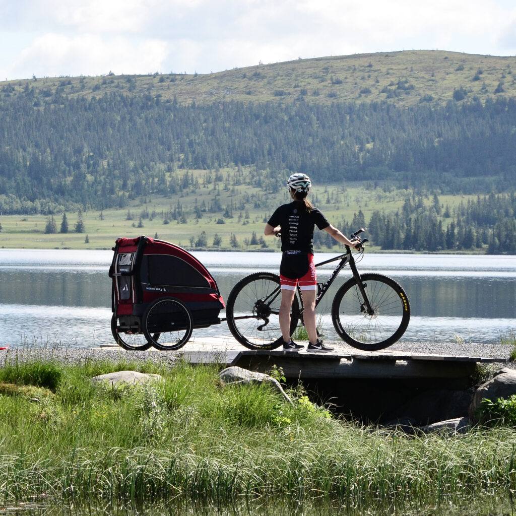 Jente står med rød sykkelvogn i norsk natur på sommer