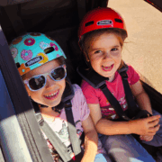 Two smiling children wearing helmets sitting in a Nordic Cab bike trailer.