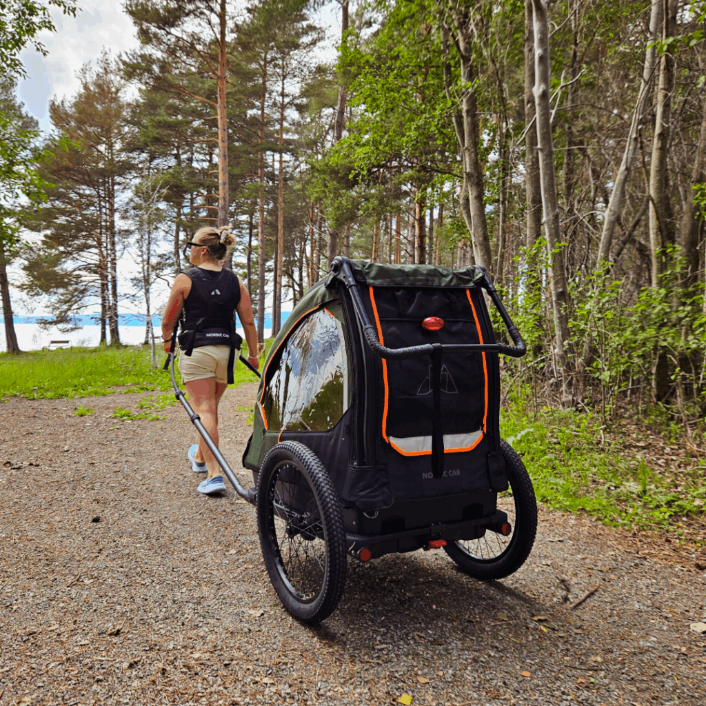 Woman pulling a Nordic Cab bike trailer with harness through the forest.