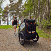 Woman pulling a Nordic Cab bike trailer with harness through the forest.