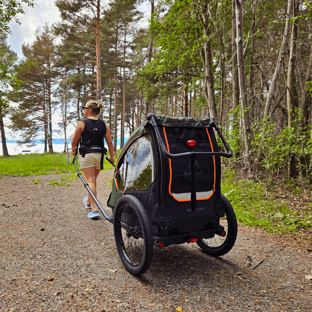 Woman pulling a Nordic Cab bike trailer with harness through the forest.