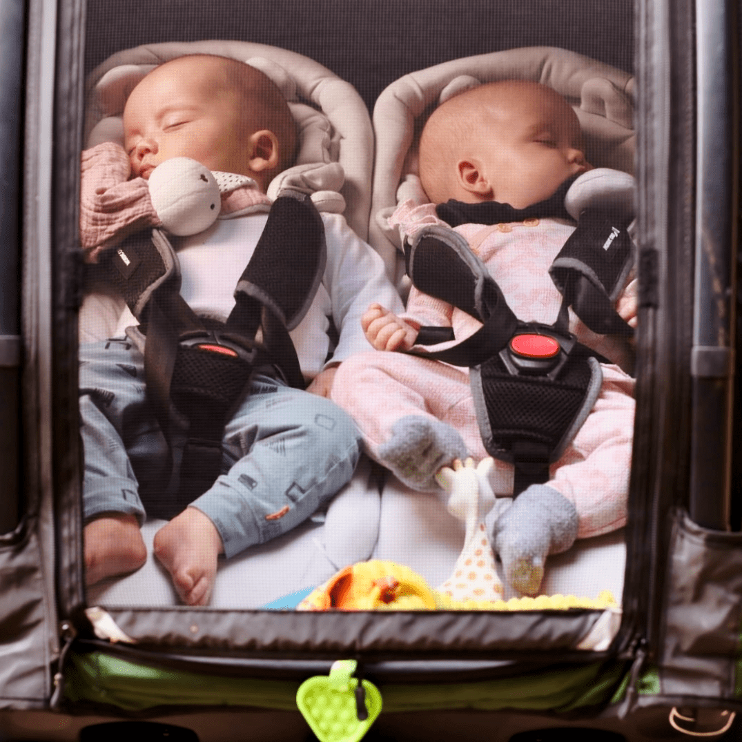 Two babies sleeping peacefully in Nordic Cab bike trailer with net cover.