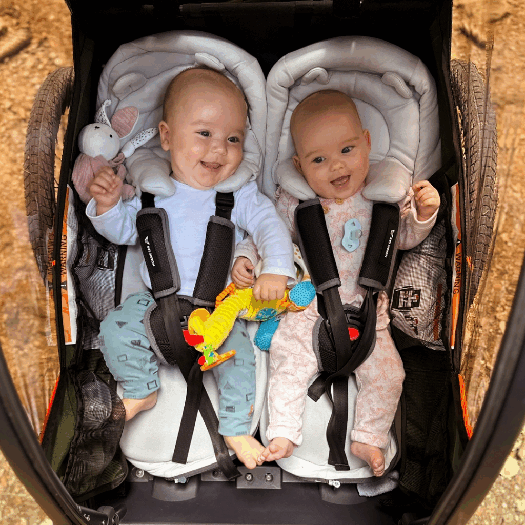 Two smiling babies in infant inserts inside a Nordic Cab bike trailer.