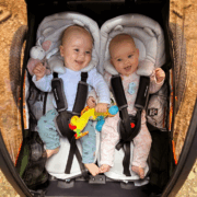Two smiling babies in infant inserts inside a Nordic Cab bike trailer.