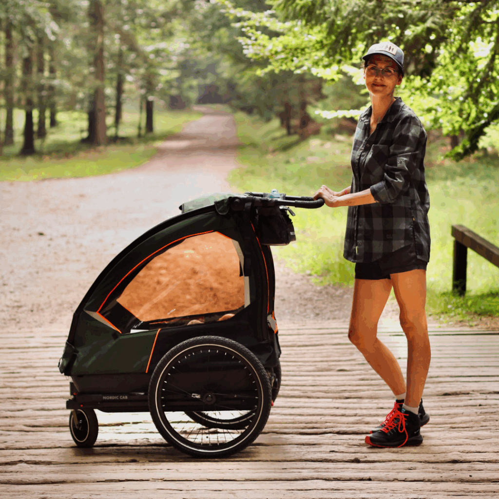 Woman pushing a Nordic Cab bike trailer in stroller mode across a wooden bridge.