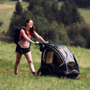 Woman pushing a Nordic Cab bike trailer through grassy terrain.